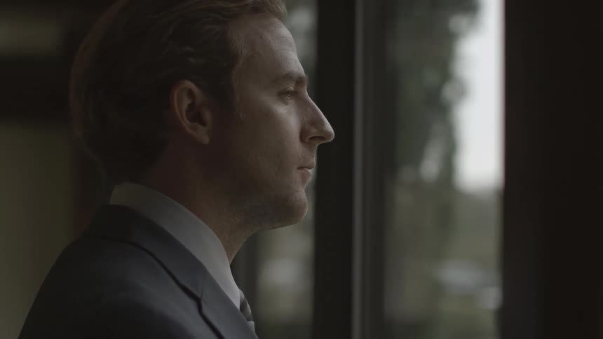 A man in a suit jacket drinking coffee and looking out a window