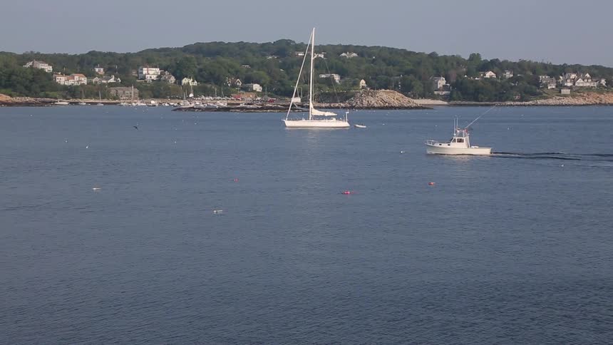 Small boat moving across the water in front of a sailboat