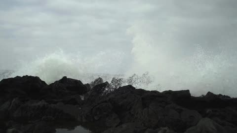 Waves crashing into and over rocks on a cloudy day