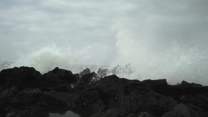 Waves crashing into and over rocks on a cloudy day
