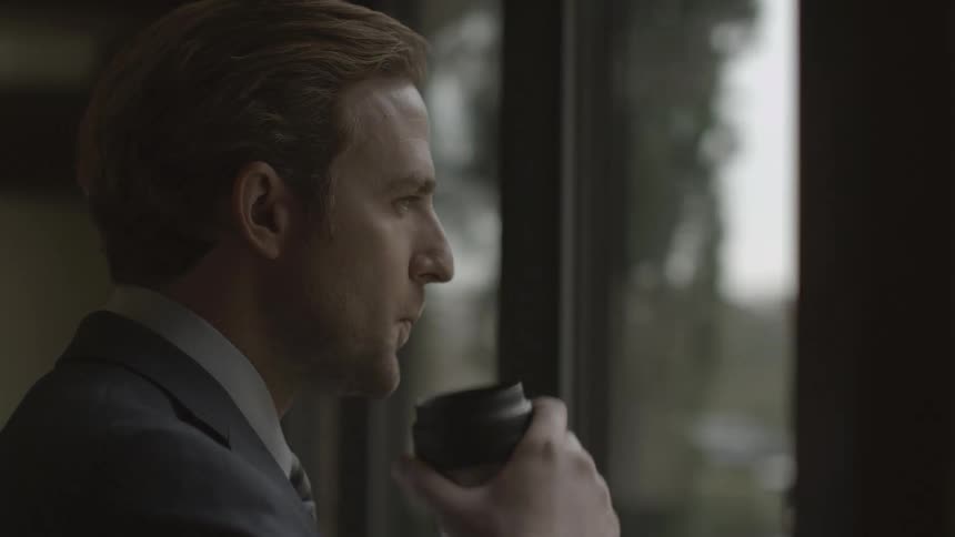 Man wearing a suit drinking coffee looking out a window