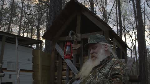 A man with a long, white beard smokes in a forest