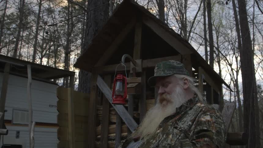 A man with a long, white beard smokes in a forest