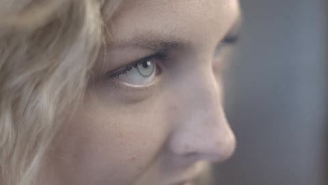 A young, blonde woman sits with her eyes closed, opens them and begins to smile and laugh