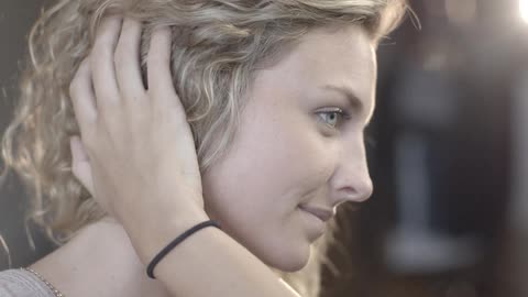 A woman brushing her curly blonde hair out of her face