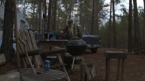 A man carries a box to a table outside of a camper in the woods
