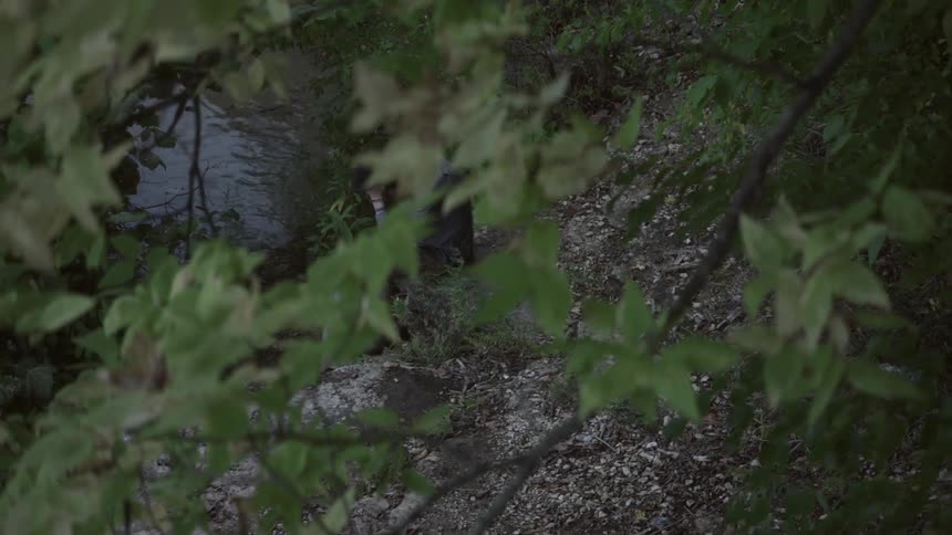 A man sits on a rock near a creek