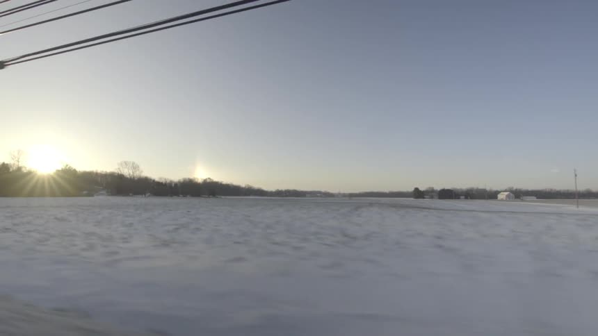 Driving on a road, passing snow-covered fields and houses