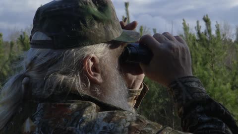 Bearded man in camo looks through binoculars