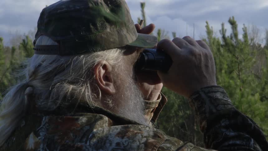 Bearded man in camo looks through binoculars