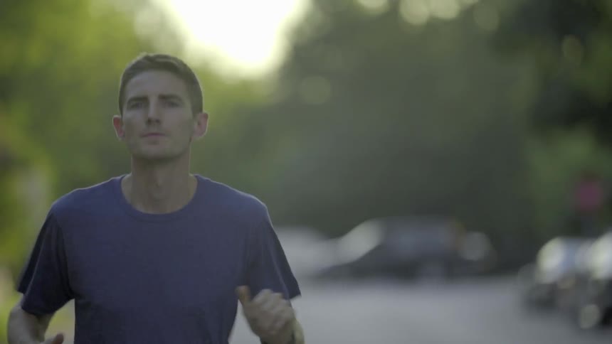 A young man jogs in a t-shirt on a neighborhood street