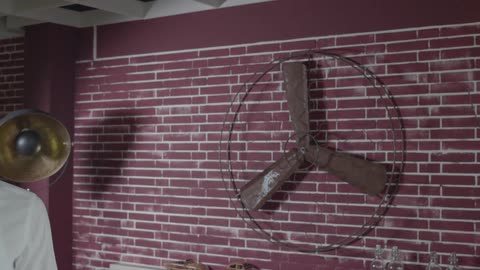 A man reading some papers while sitting on a couch located in front of a red brick wall before getting up to look out of the windows
