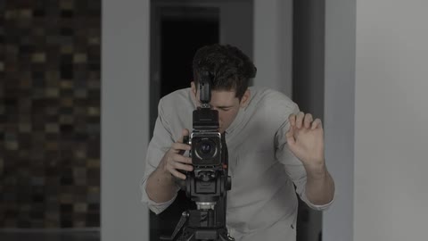 A man stands behind a professional camera and holds up his fingers for a countdown