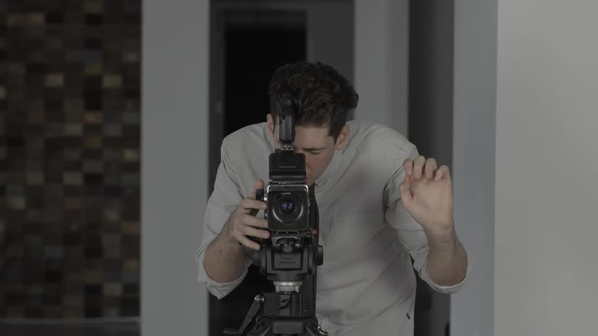 A man stands behind a professional camera and holds up his fingers for a countdown