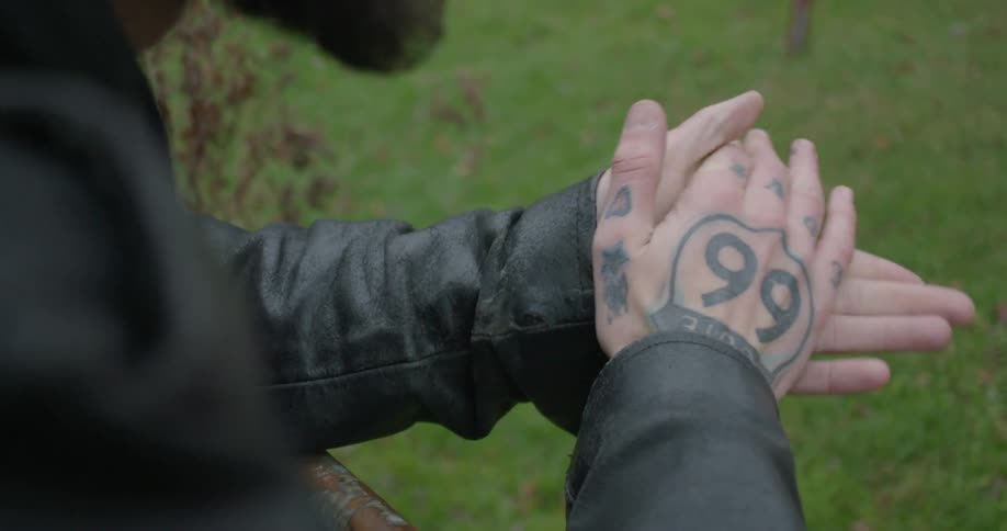A leather-clad man rubbing his tattooed hands together