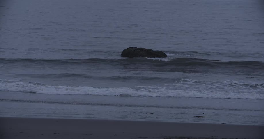 Waves crashing around a rock and onto a beach