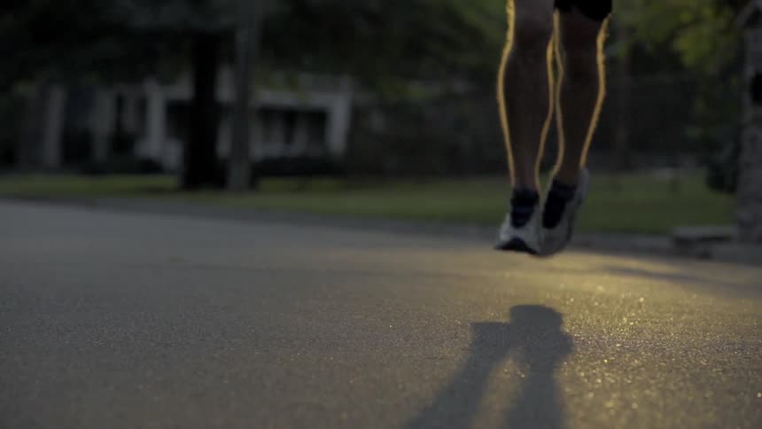 A man jogging down a street with a lawn and white house in the background