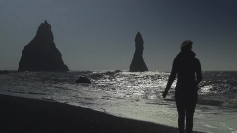 A woman walks down a beach at dusk