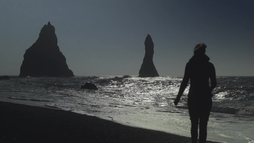 A woman walks down a beach at dusk
