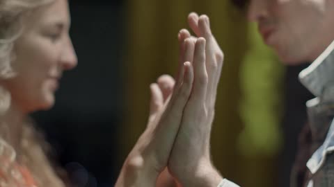 A man and woman facing each other are holding their hands out palms forward touching their palms together