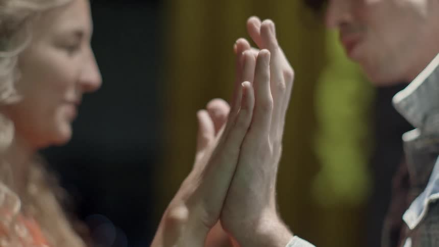 A man and woman facing each other are holding their hands out palms forward touching their palms together