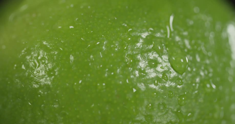 A macro view of a green fruit with beads of water trickling down its sides
