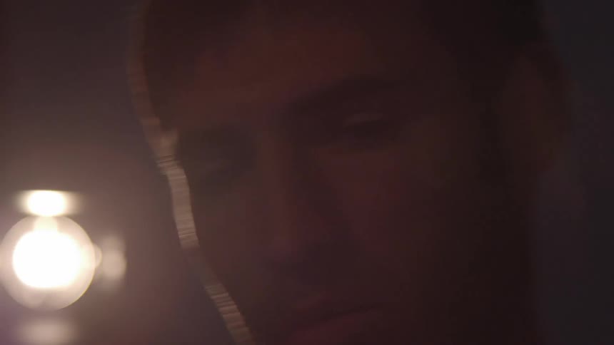 A man in dim lighting is intently working on something out of camera view