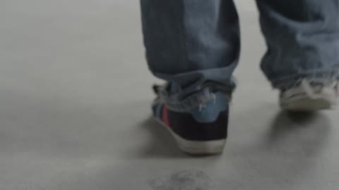 The feet of a young man walking while wearing well-worn jeans and sneakers