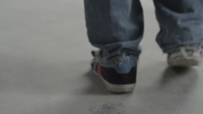 The feet of a young man walking while wearing well-worn jeans and sneakers