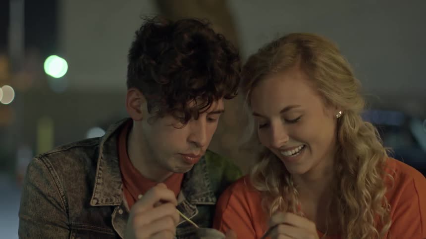 A man and a woman sitting outside at night and sharing a bowl of food