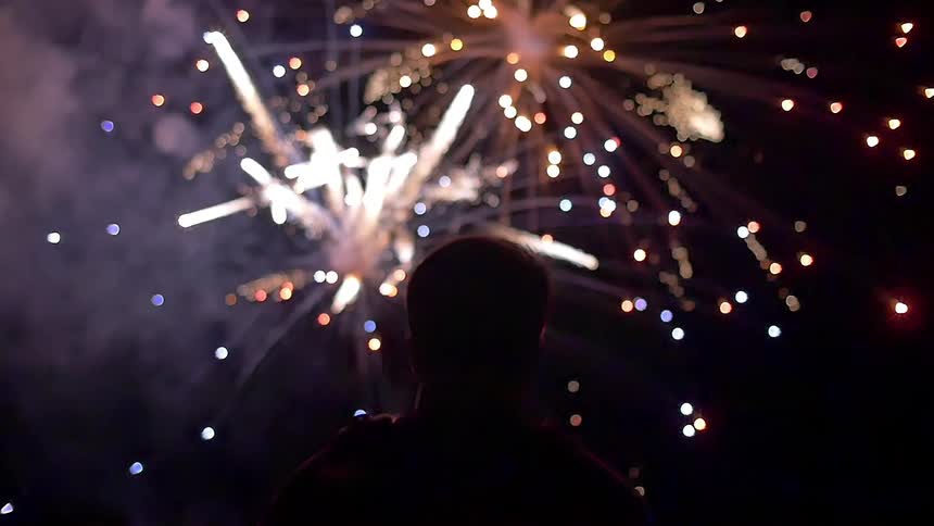 A man standing out and watching the fireworks on a dark night
