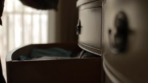 A person opens a dresser drawer and rummages through clothes