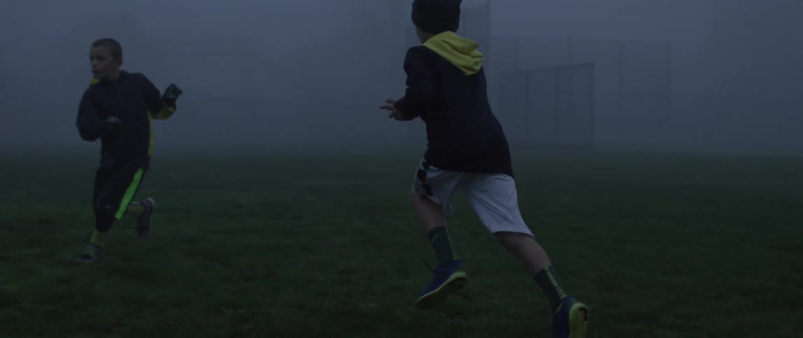 Young boys play football in the fog on a playground at dusk