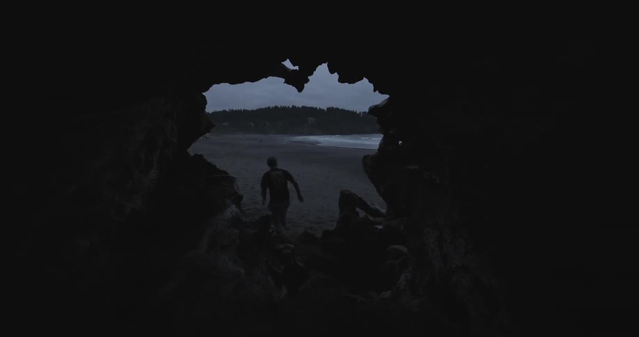 A man exits a dark cave onto a beach