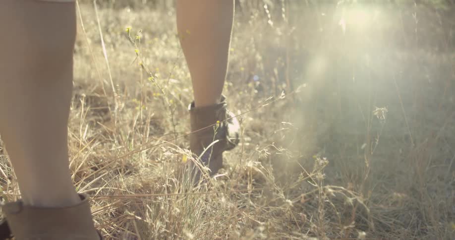 A woman in boots walks through a grassy field