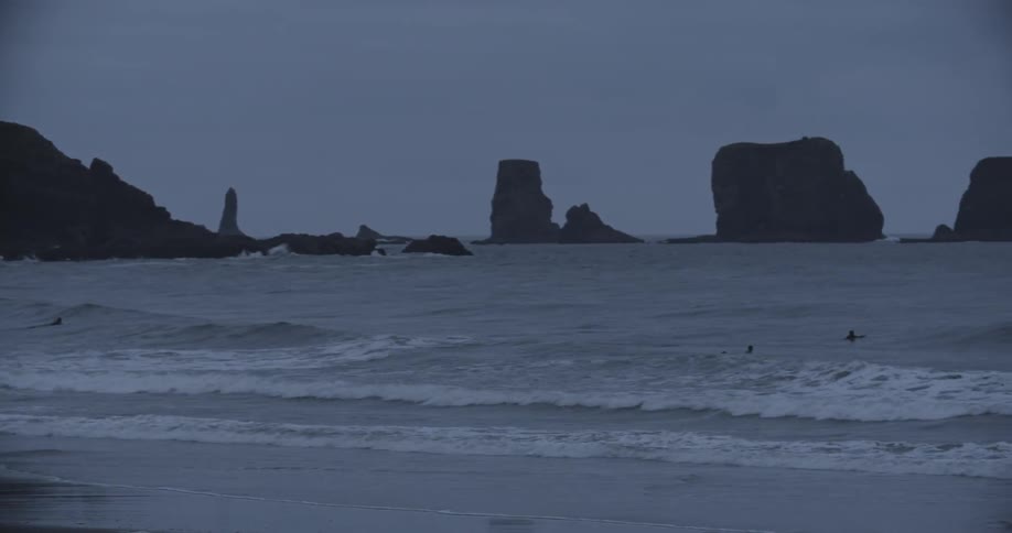 Waves crashing in the ocean as people swim in the water at dusk