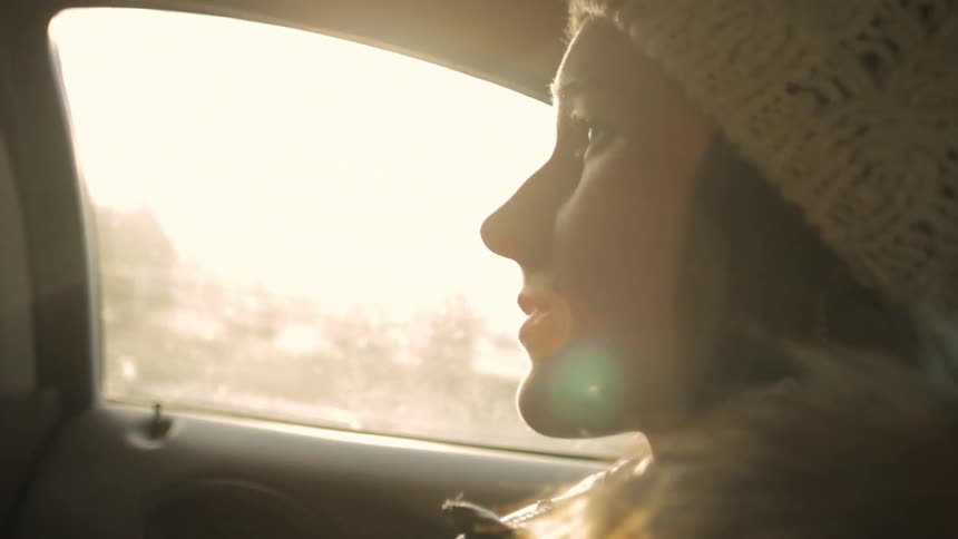 A young, brunette woman riding in a car and talking