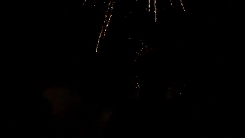 Fireworks explode in the night sky while a man stands watching