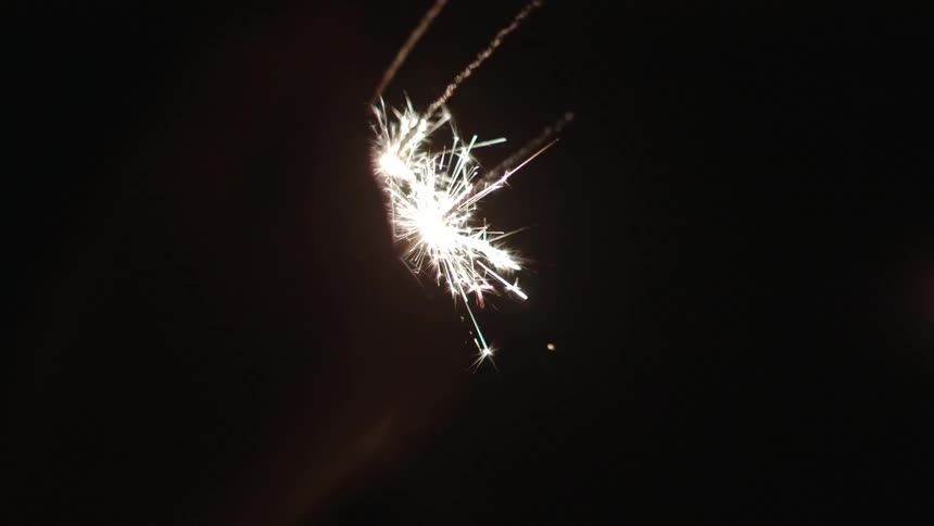 A hand holding sparklers that have burned low in the dark