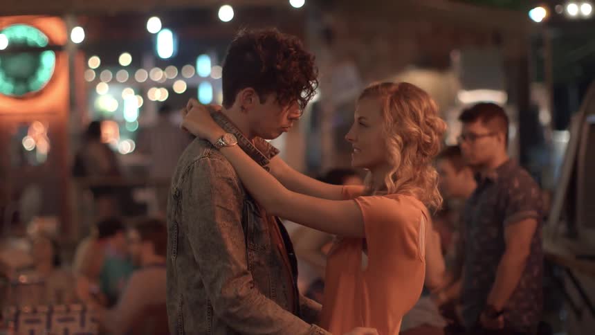 A young man and woman are slow dancing while the woman talks to the man at a restaurant