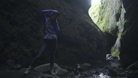 A woman taking pictures next to a river running between steep cliffs