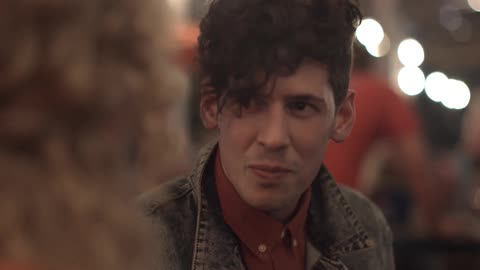 A man in a denim jackets laughs and chats with another person