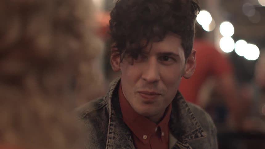 A man in a denim jackets laughs and chats with another person