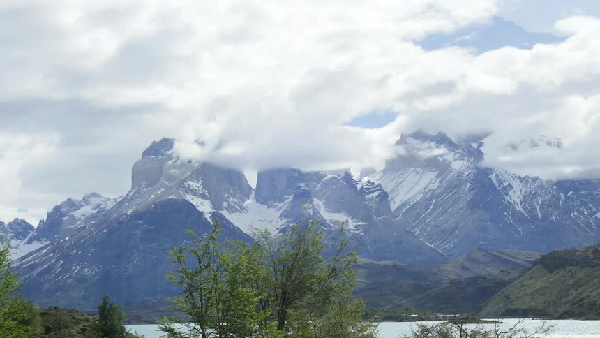 Clouds blowing over snow-capped mountains behind a lake