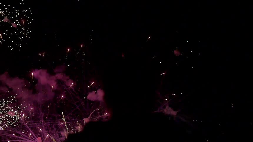 A person is silhouetted while viewing a busy fireworks display at night