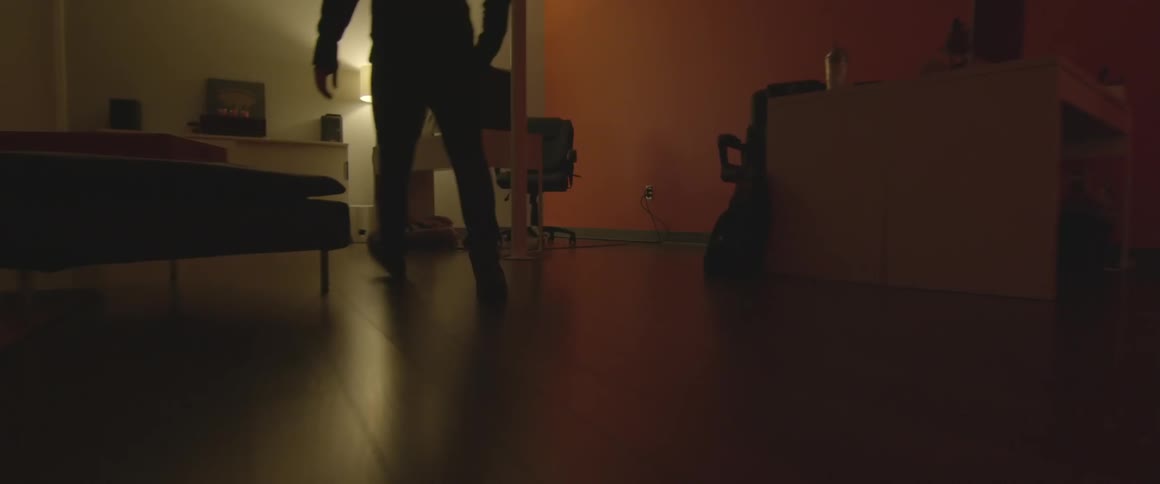 A man walking through a bedroom, crouching in front of a cabinet and opening it
