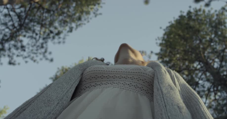 A woman in a sweater looks upwards towards the treetops