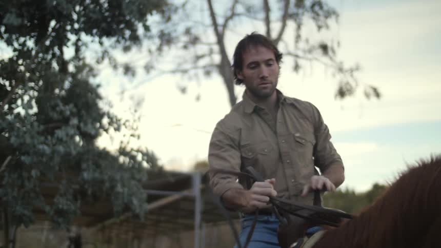 A man mounting a horse on a farm at sunset