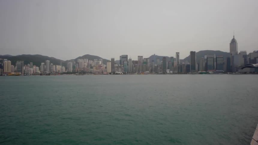 A skyline with water and people walking down a walkway beside the water on a cloudy day