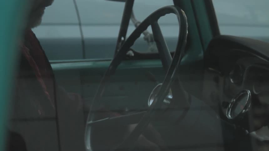 A man behind the steering wheel of an older vehicle and starting the engine at dusk